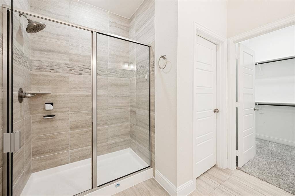 12986 Jk Ojha Street, Farmers Branch, TX 75234 Shower enclosure with glass doors, a rainfall showerhead, and a tiled surround with decorative accents