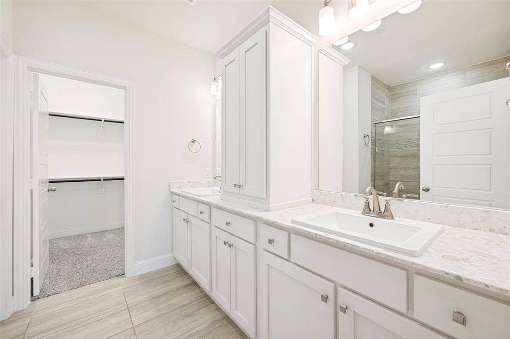 12986 Jk Ojha Street, Farmers Branch, TX 75234 Bathroom featuring dual rectangular sinks set into stone-finish countertops, extensive white cabinetry, a large vanity mirror, and tile flooring