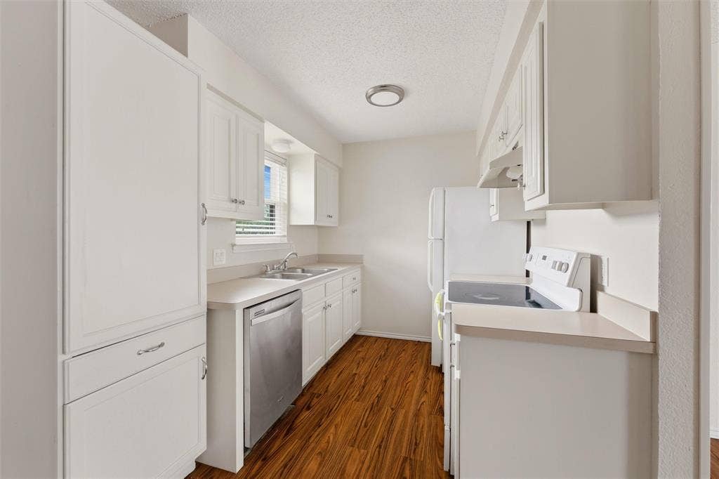 401 N 7th Street, Midlothian, TX 76065 Bright kitchen featuring white cabinetry, light countertops, wood-finish flooring, a stainless steel dishwasher, and a window for natural light