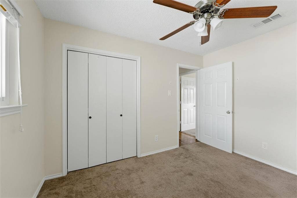 401 N 7th Street, Midlothian, TX 76065 Carpeted room featuring a ceiling fan with wood-finish blades, a window with blinds, and white bi-fold closet doors