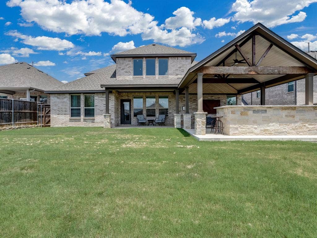 1021 Daylily Drive, Northlake, TX 76226 Expansive backyard featuring a covered patio, vaulted outdoor living area with a ceiling fan, stone-clad outdoor kitchen, and a privacy fence