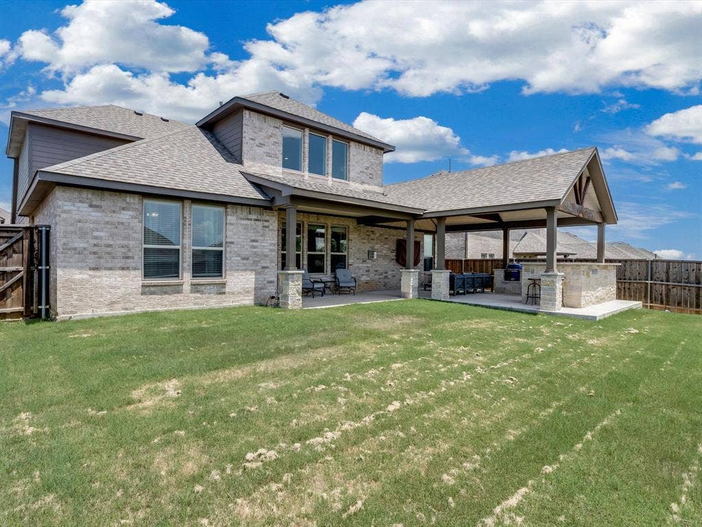 1021 Daylily Drive, Northlake, TX 76226 Rear exterior featuring a covered patio, outdoor kitchen, stone accent columns, brick and siding facade, and a fenced perimeter