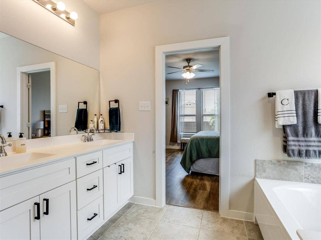1021 Daylily Drive, Northlake, TX 76226 Bathroom vanity featuring dual sinks, white cabinetry with black hardware, and an expansive mirror