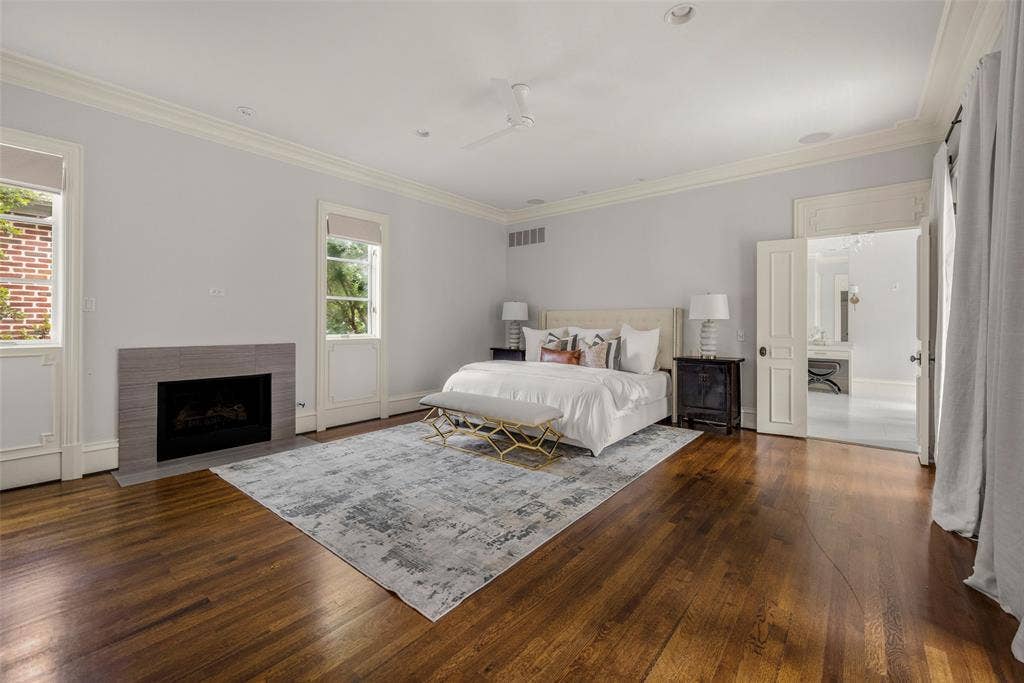 Spacious interior with rich wood-finish flooring, a modern fireplace, crown molding, double windows, and access to an adjoining room