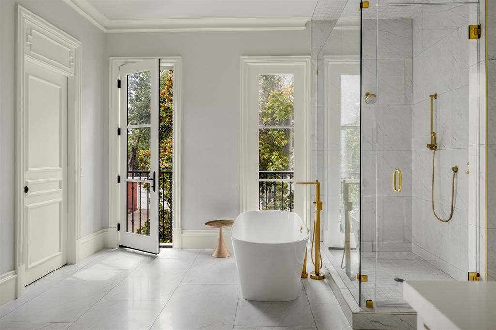 Spacious bathroom featuring a freestanding soaking tub with a floor-mounted gold-tone faucet, a glass-enclosed shower with gold-tone fixtures, and white tiled flooring