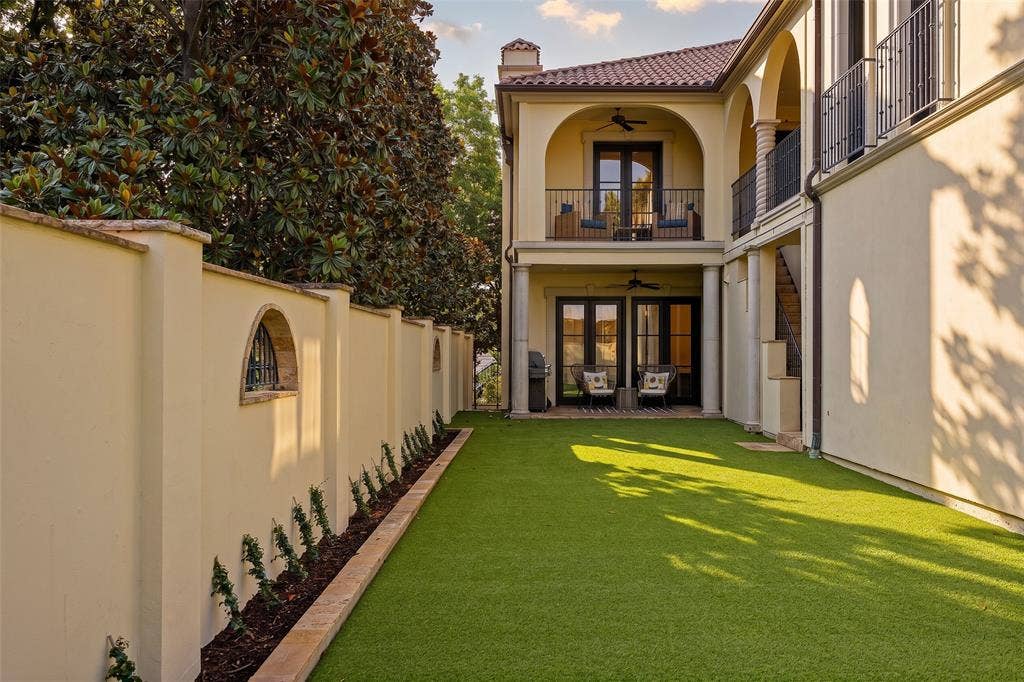 Spacious backyard featuring artificial turf, a stucco privacy wall with arched details, and mature trees