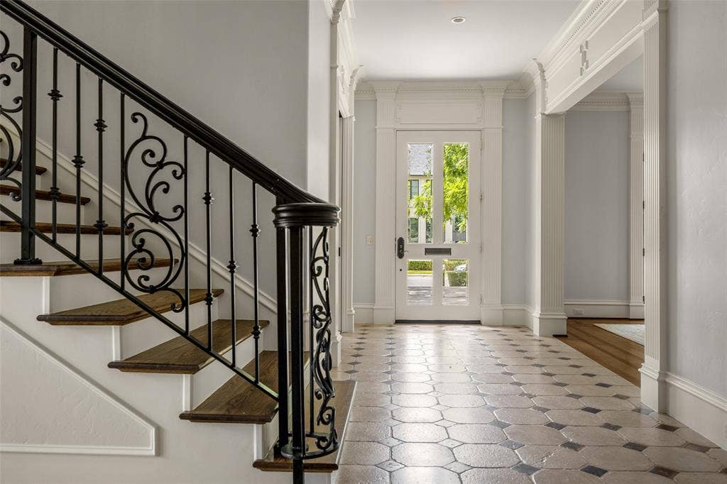Entryway featuring an ornate wrought iron staircase, wood-finish treads, a decorative glass-paneled entry door, geometric tile flooring, and extensive crown molding