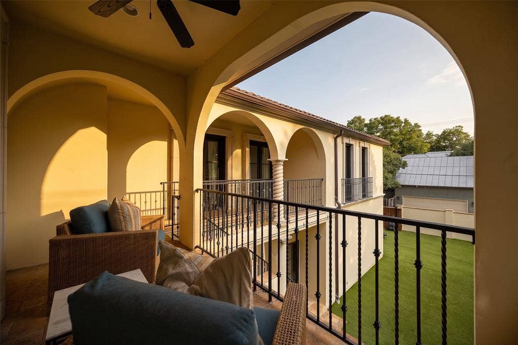 Expansive outdoor balcony featuring multiple architectural arches, decorative wrought iron railings, a built-in ceiling fan, and a view of the manicured lawn below