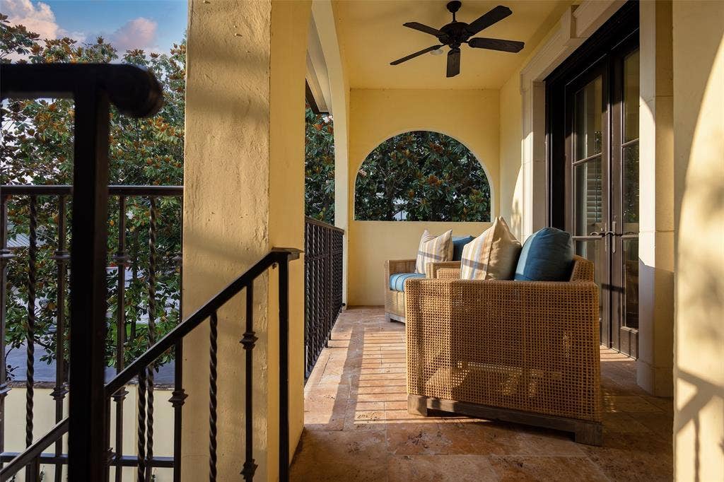 Covered outdoor balcony featuring a stone tile floor, stucco walls, black metal railings, and a ceiling fan