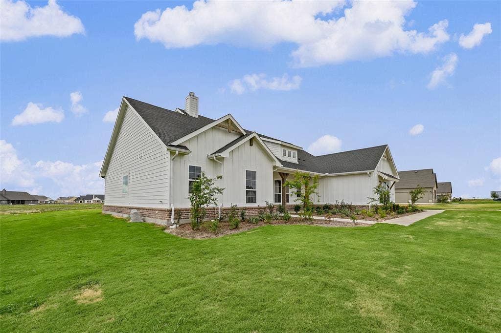 12413 Hornfels Drive, Krum, TX 76249 White siding exterior with dark shingle roofing, brick foundation, and established landscaping