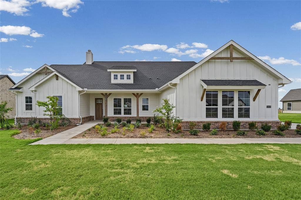 12413 Hornfels Drive, Krum, TX 76249 White board-and-batten exterior with brick skirting, dark shingle roof, and a wood-finish front door
