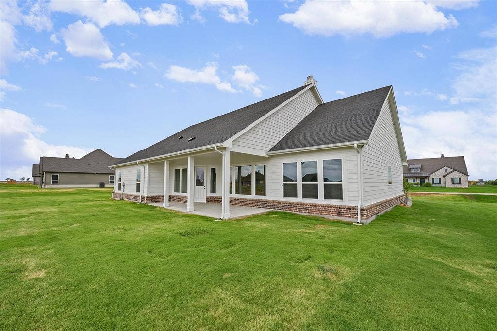 12413 Hornfels Drive, Krum, TX 76249 Expansive rear lawn, covered patio, white siding exterior, brick foundation, and dark shingle roof