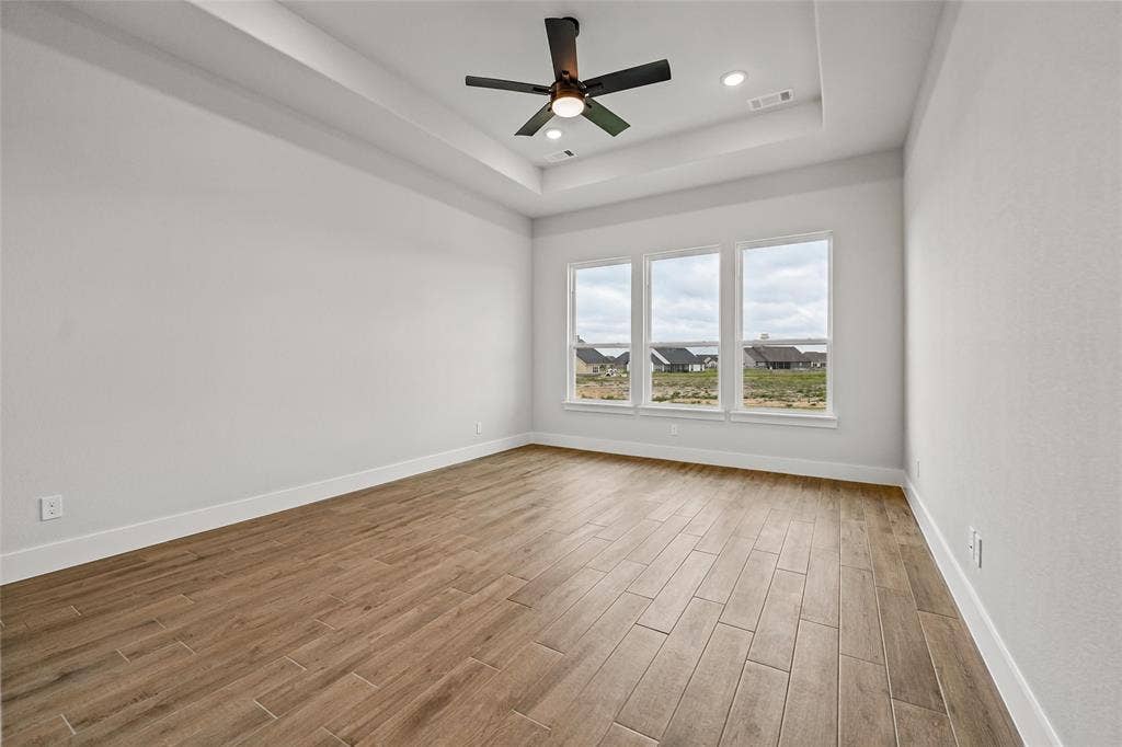 12413 Hornfels Drive, Krum, TX 76249 Tray ceiling with recessed lighting and a ceiling fan, three large windows, and wood-finish flooring