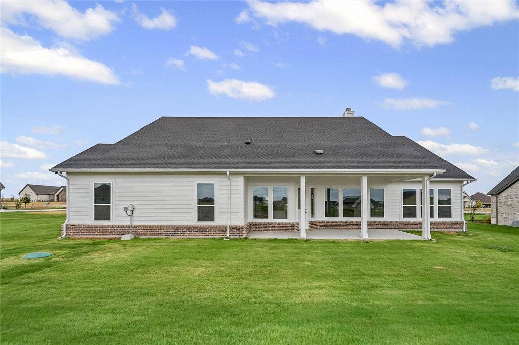 12413 Hornfels Drive, Krum, TX 76249 Expansive green lawn, covered patio, brick and siding exterior, multiple windows, and a dark shingle roof