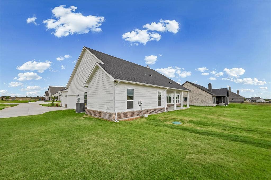 12413 Hornfels Drive, Krum, TX 76249 Exterior featuring white siding, dark shingle roofing, a partial brick facade, and a covered back patio with white columns