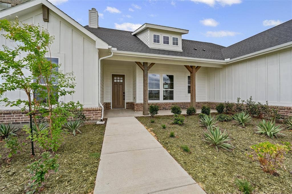 12413 Hornfels Drive, Krum, TX 76249 Inviting facade featuring a covered entry, board and batten siding, brick wainscoting, a dark wood-finish front door, and a dormer window