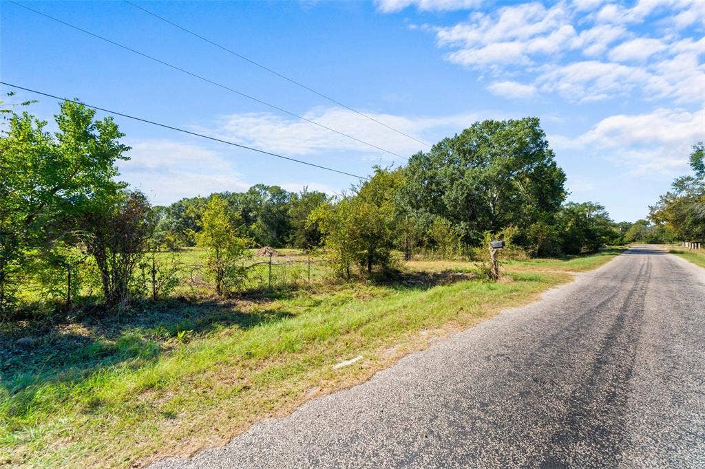 11691 Betty Lane, Kaufman, TX 75142 Roadside property featuring a paved road, green grass, mature trees, and a wire fence