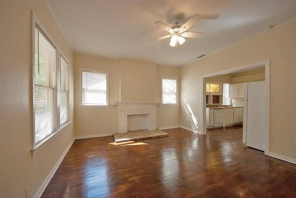 5405 Worth Street, Dallas, TX 75214 A spacious living room featuring hardwood floors, several windows, a fireplace and a ceiling fan, creating a bright and airy atmosphere.