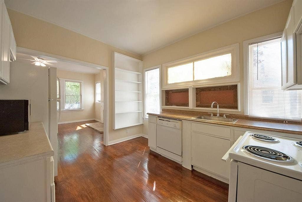 5405 Worth Street, Dallas, TX 75214 A cozy kitchen with white cabinets and shelves, a microwave, dishwasher and a stove, creating a clean and inviting cooking space.