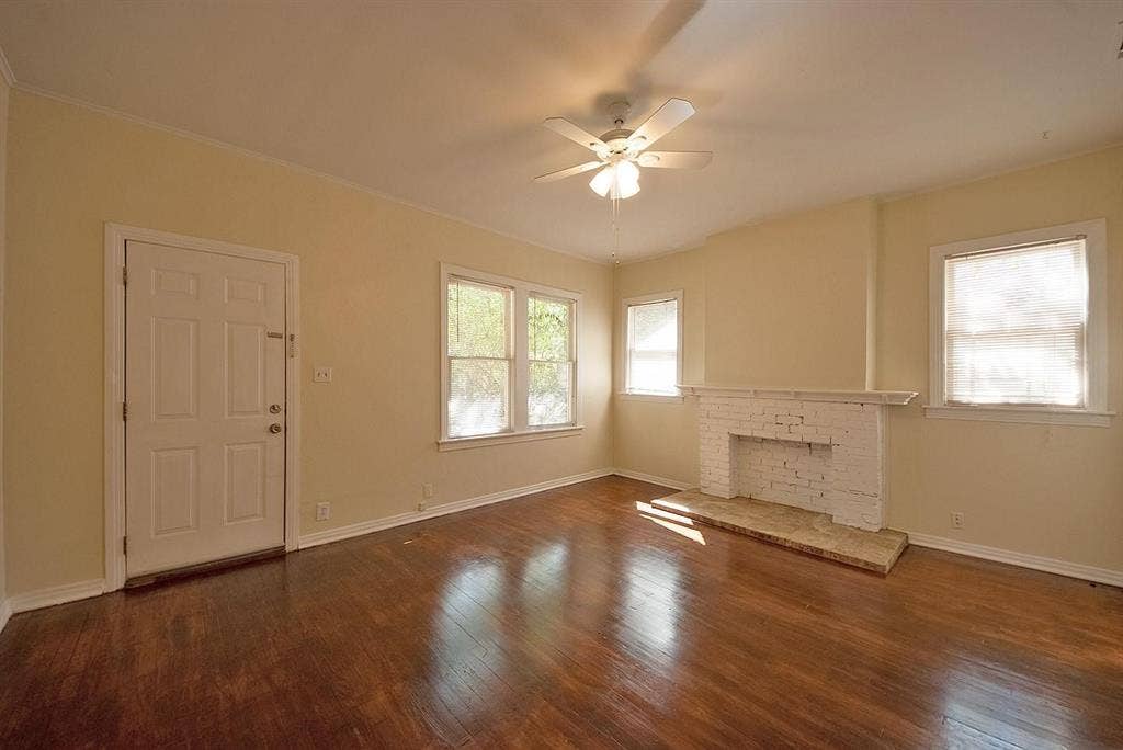 5405 Worth Street, Dallas, TX 75214 A spacious living room featuring hardwood floors, several windows, a fireplace and a ceiling fan, creating a bright and airy atmosphere.