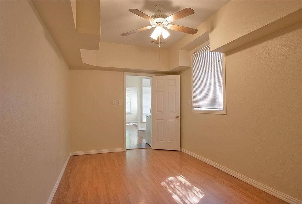 5405 Worth Street, Dallas, TX 75214 A cozy bedroom with a window featuring hardwood floors and a ceiling fan, perfect for keeping cool and comfortable.