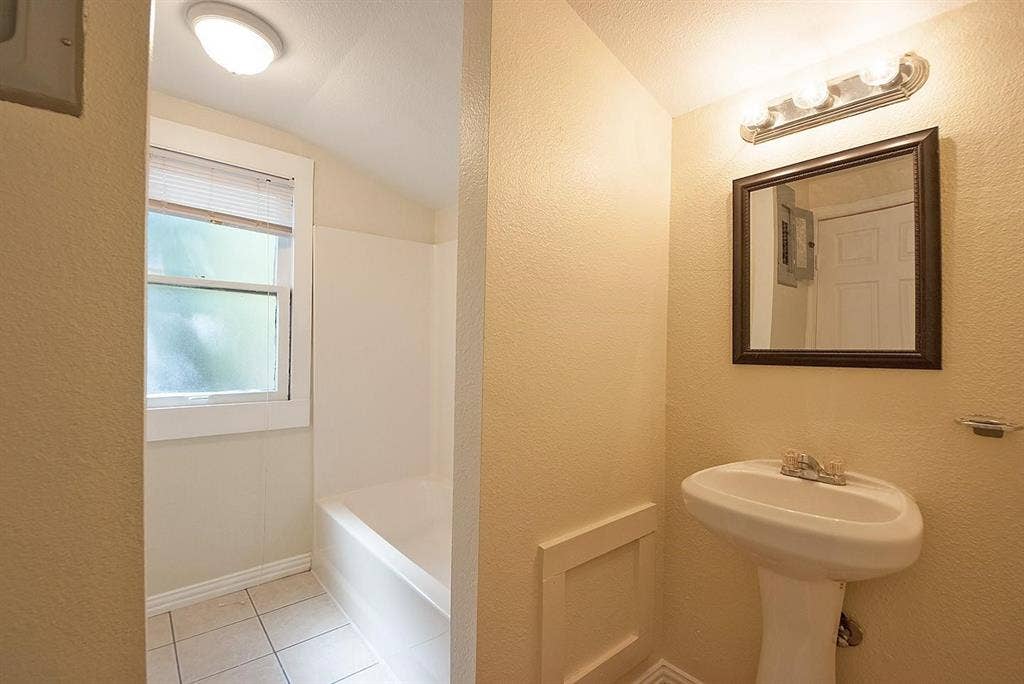 5405 Worth Street, Dallas, TX 75214 A bright bathroom with a sink, bathtub, and a window for ventilation and natural light.