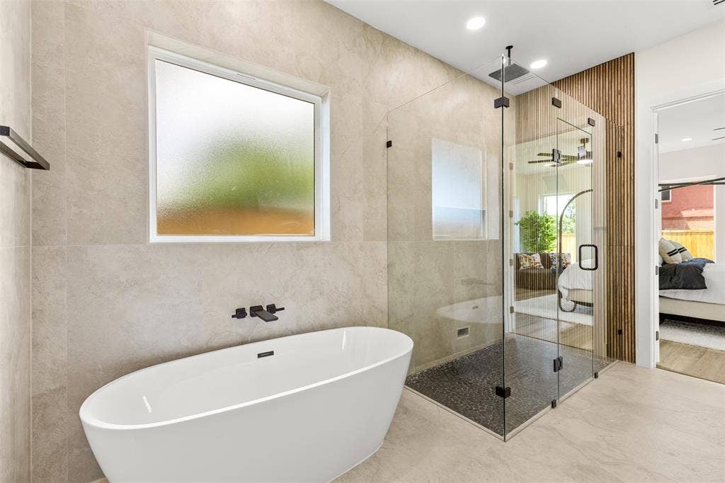 1407 Pueblo Street, Dallas, TX 75212 Contemporary bathroom featuring a freestanding soaking tub with wall-mounted matte black fixtures, a spacious glass-enclosed shower with a rainfall showerhead and dark pebble flooring, and a decorative vertical wood slat accent wall