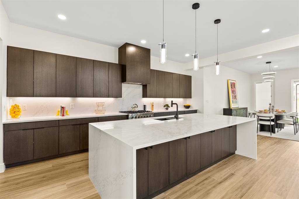 1407 Pueblo Street, Dallas, TX 75212 Modern kitchen featuring a large center island with a white countertop, dark wood-finish cabinetry, integrated stainless steel appliances, and wood-finish flooring