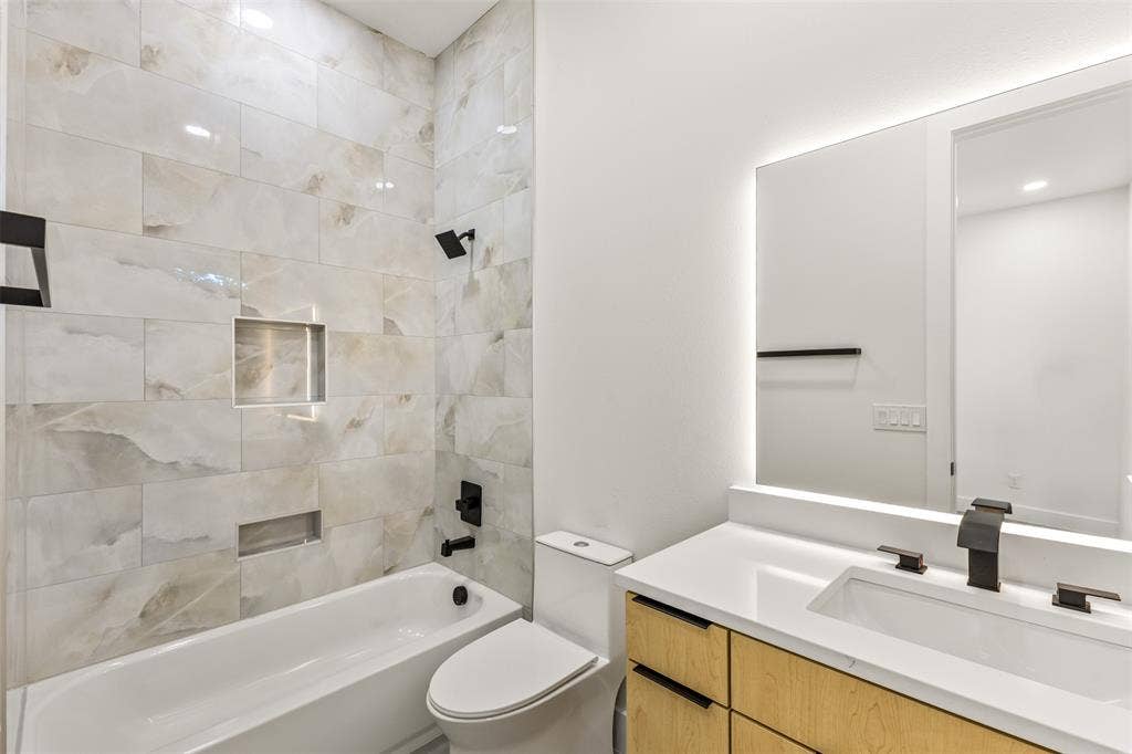 1407 Pueblo Street, Dallas, TX 75212 Contemporary bathroom featuring a tub/shower combination with tiled surround, a built-in shower niche, a floating wood-finish vanity with a white countertop, and an illuminated mirror