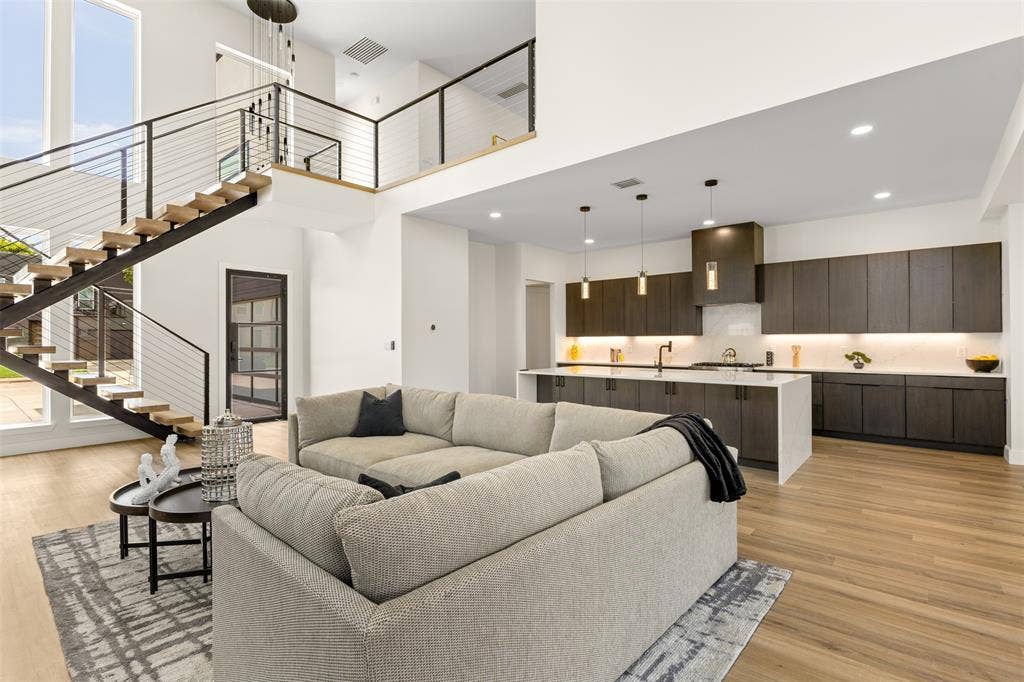 1407 Pueblo Street, Dallas, TX 75212 Open-concept living space featuring a floating staircase with cable railing, wood-finish flooring, a kitchen with dark cabinetry, a center island, and integrated lighting