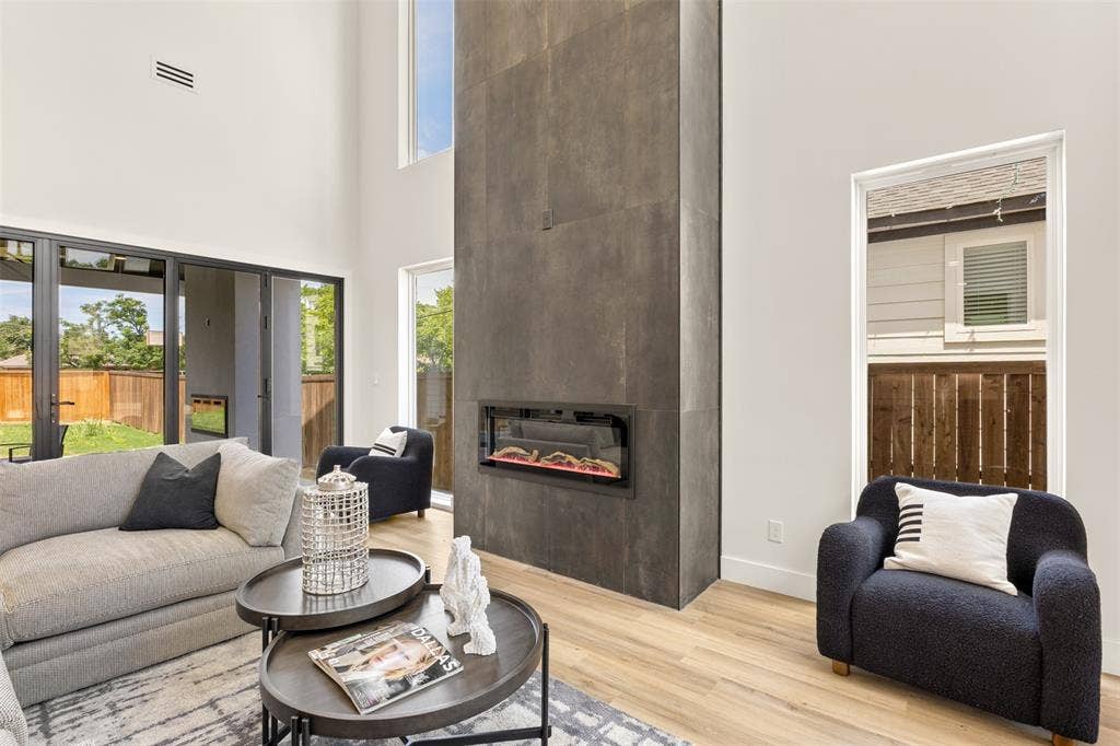 1407 Pueblo Street, Dallas, TX 75212 Expansive living area featuring a floor-to-ceiling fireplace with an integrated linear firebox, soaring ceilings, light wood-finish flooring, and large glass sliding doors providing abundant natural light