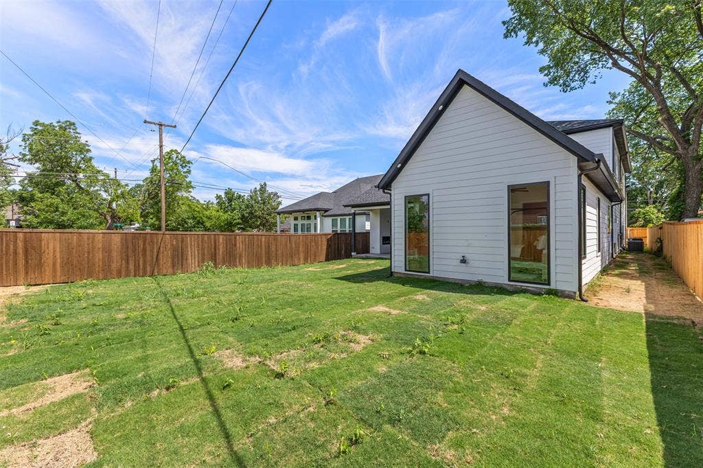 1407 Pueblo Street, Dallas, TX 75212 Contemporary white siding exterior with a dark-trimmed roofline, complemented by tall, black-framed windows, a private wood fence, and a green grass area