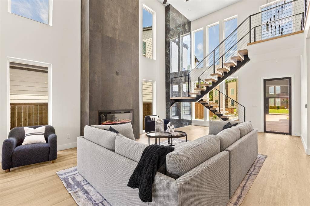 1407 Pueblo Street, Dallas, TX 75212 Two-story living area featuring a prominent fireplace wall, a floating staircase with cable railing, high ceilings, abundant natural light from multiple windows, and light wood-finish flooring