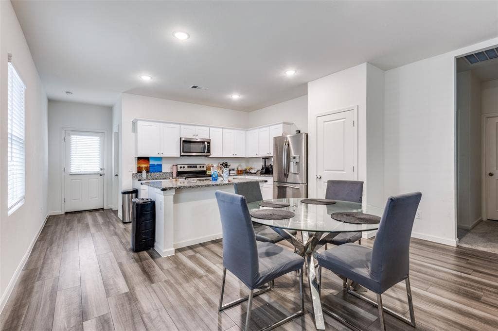 Open-concept kitchen and dining area featuring wood-finish flooring, white cabinetry, granite-style countertops, stainless steel appliances, and recessed lighting