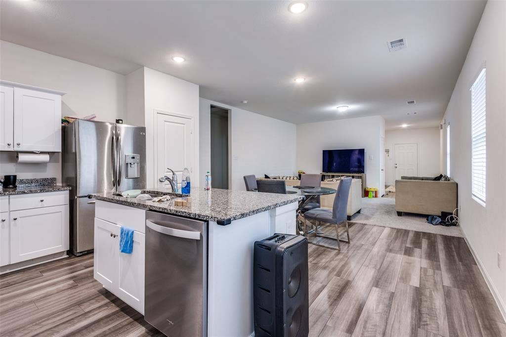 Open-concept living space featuring a kitchen island with stone countertops, stainless steel appliances, white cabinetry, recessed lighting, and wood-finish flooring