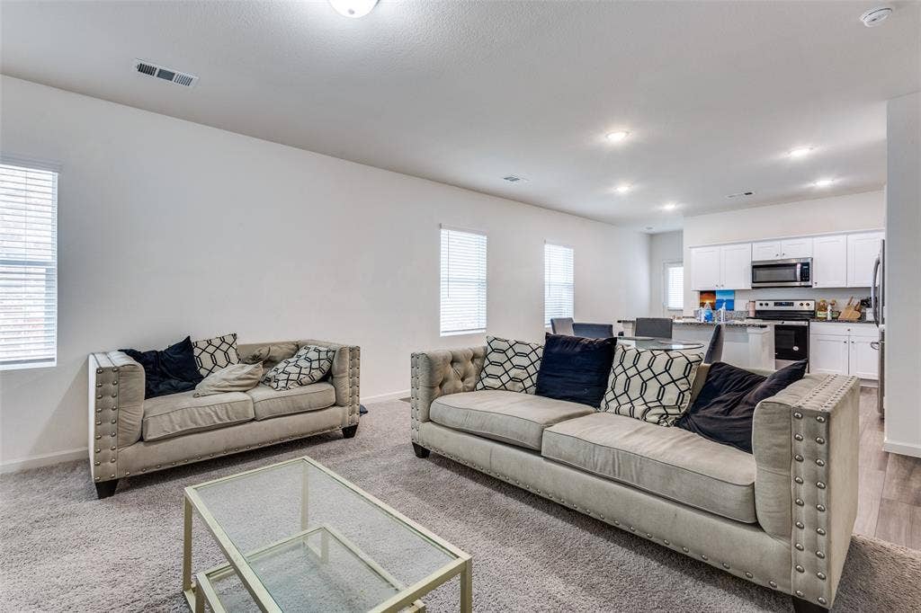 Open-concept living space featuring light gray carpeting, recessed lighting, and multiple windows with blinds