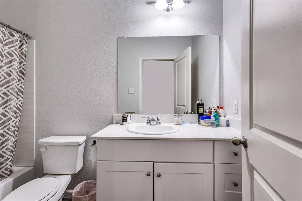 Bathroom featuring a white vanity with integrated sink, a large wall-mounted mirror, brushed nickel hardware, and a tub with tiled surround
