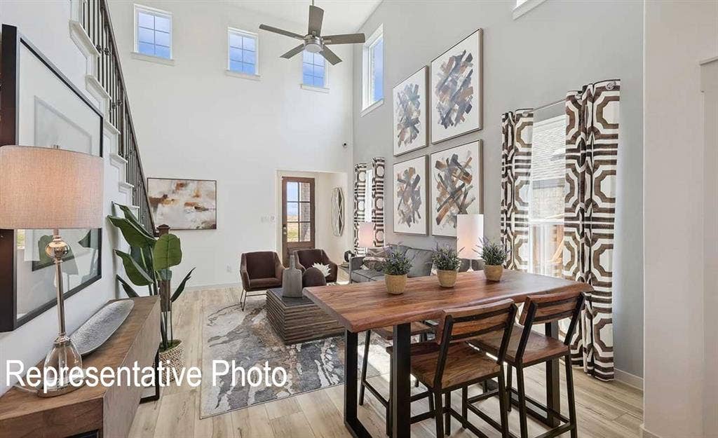 Two-story living area featuring a prominent staircase with dark railings, light-toned wood-finish flooring, and multiple high windows