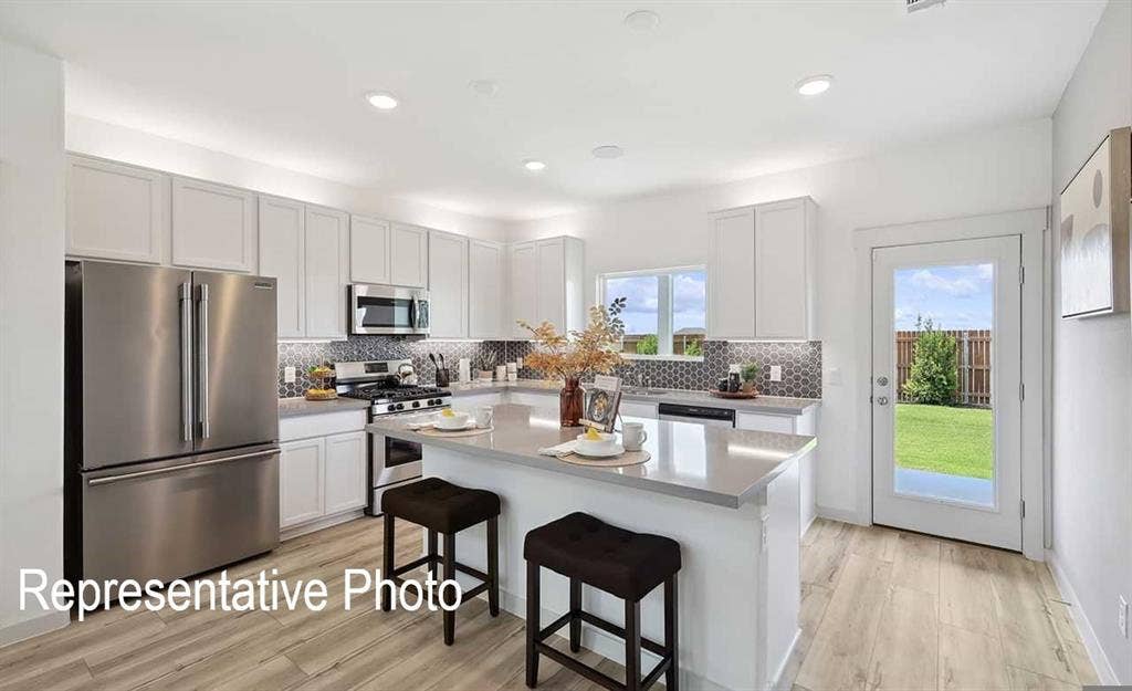 Modern kitchen featuring light wood-finish flooring, white cabinetry, stainless steel appliances, and a hexagon tile backsplash
