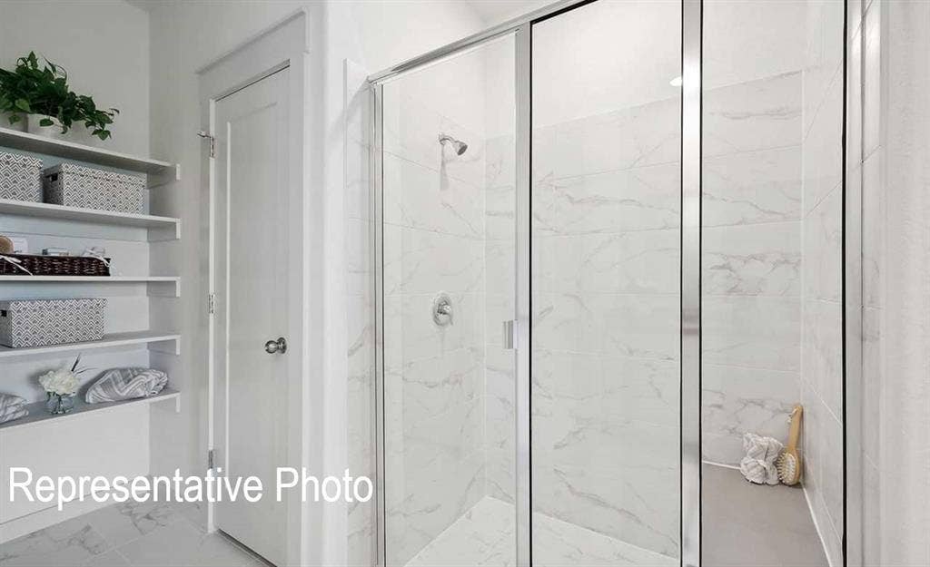 Walk-in shower with clear glass enclosure, white marble-look wall tiles, and a built-in shower niche