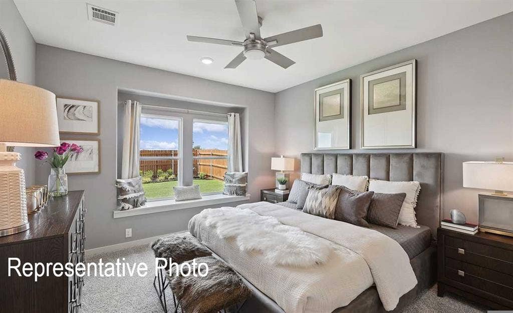 Spacious bedroom featuring plush carpeting, a large window with a built-in window seat, a contemporary ceiling fan, and ample natural light