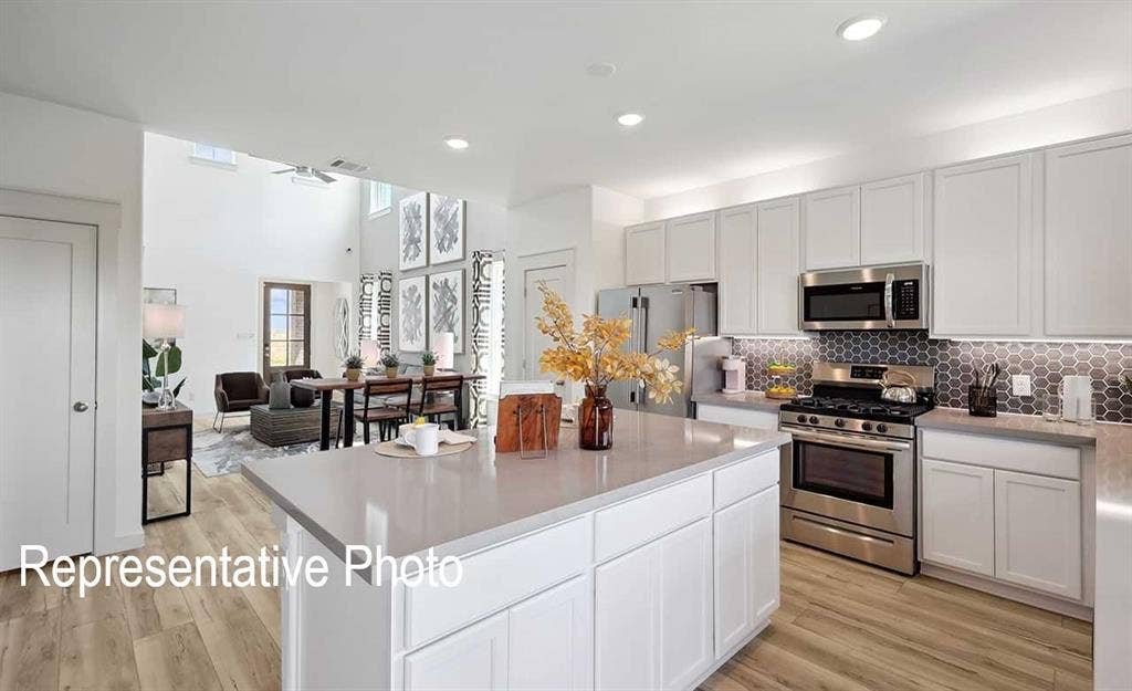 Open-concept kitchen featuring an expansive island with countertop seating, white shaker cabinetry, stainless steel appliances, and a hexagon tile backsplash