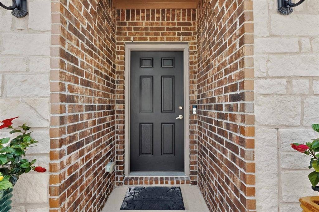 698 Langdon Street, Lavon, TX 75166 Inviting entry featuring a paneled black door, complementary light stone and brick facade, and an integrated smart doorbell system