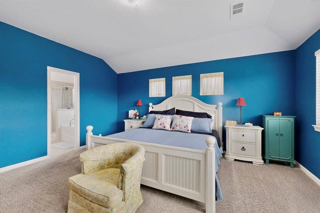 698 Langdon Street, Lavon, TX 75166 Carpeted bedroom featuring a vaulted ceiling, multiple windows with white blinds, and an entryway to a full bathroom with a shower and tub combination