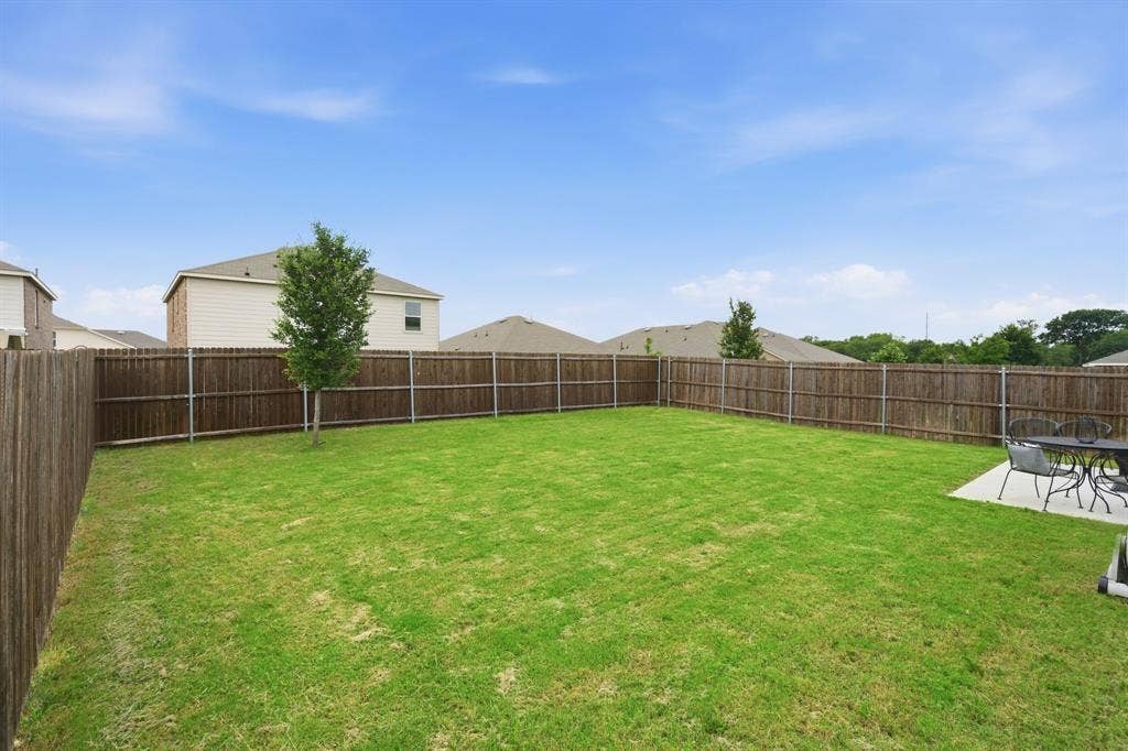 Expansive backyard featuring a lush lawn, privacy wood fencing, and a concrete patio