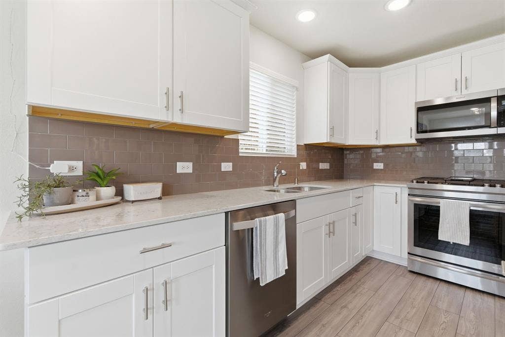 White shaker cabinetry paired with stainless steel appliances including built in microwave and gas range, a light-toned silestone quartz countertop, and a gray subway tile backsplash