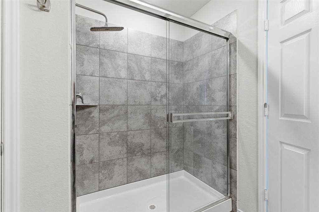Shower enclosure featuring a sliding glass door, gray tile surround, rainfall showerhead, and a built-in shower niche