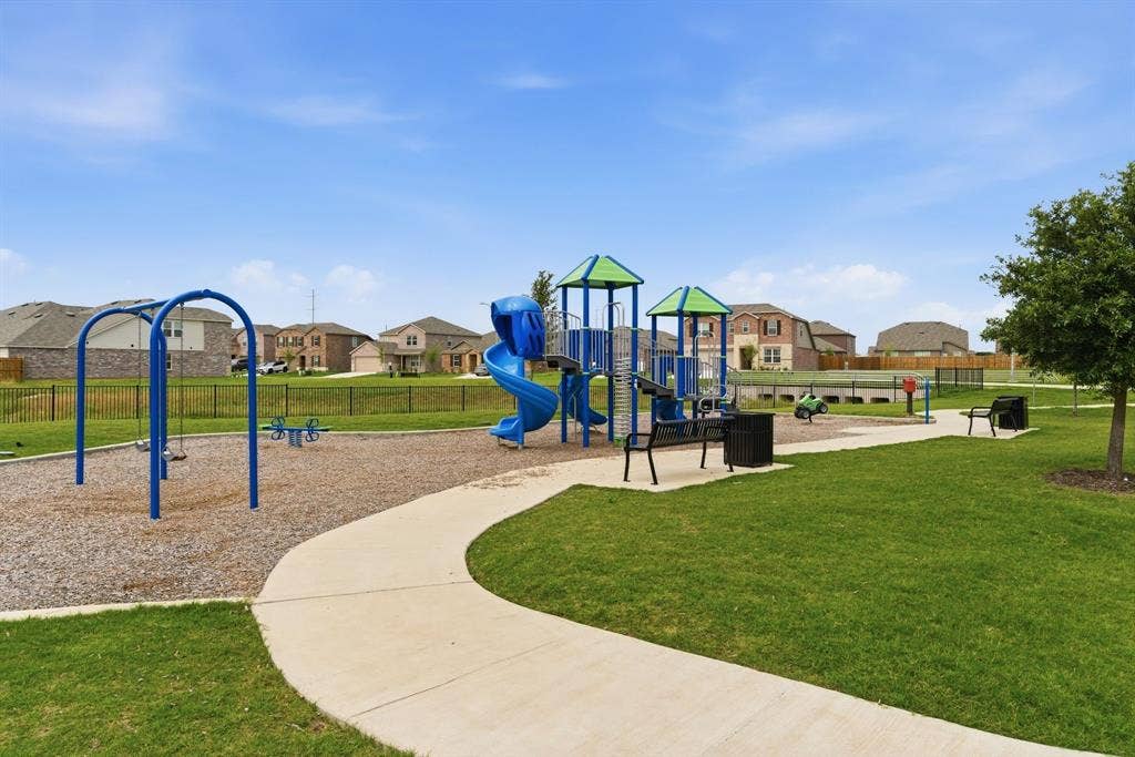 Community playground with swings, slides, and multiple play structures, bordered by a concrete pathway and green space