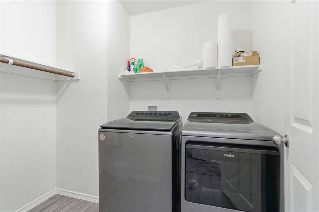 Dedicated laundry area featuring wood-look tile flooring, a wall-mounted shelving unit, and a clothes hanging rod