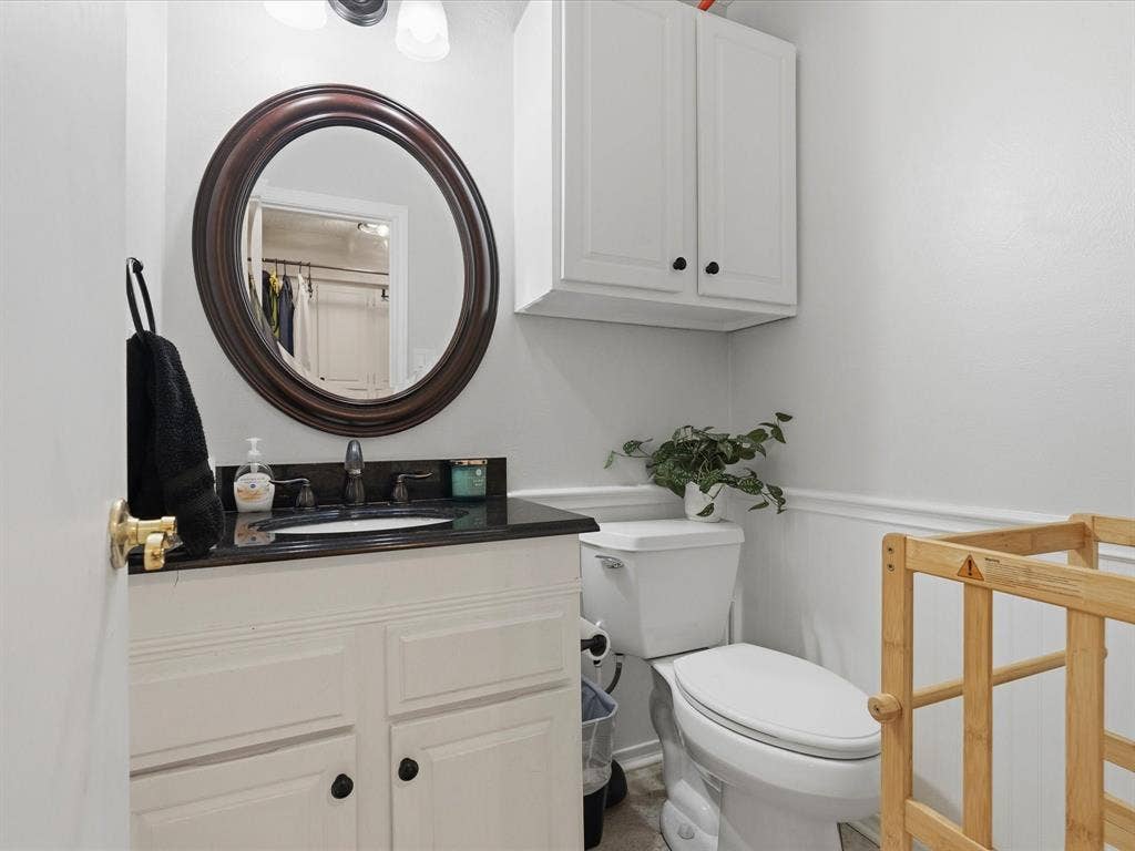 2812 Prescott Drive, Carrollton, TX 75006 Bathroom featuring a white vanity with dark countertop, an oval mirror with a dark wood-finish frame, and white wall-mounted cabinetry